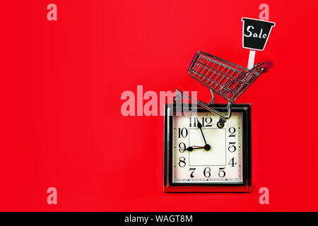 Christmas Black Friday Sale concept with silver clock, shopping cart shop trolley with sign sale on red background. Stock Photo