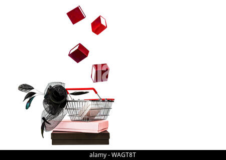 Shopping basket with female hat with veil and feather in retro style and flying falling red gift boxes on white background, isolated. Stock Photo