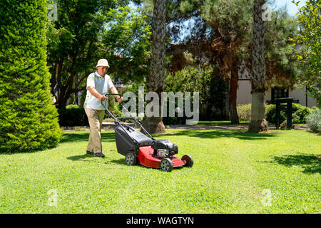 Old gardener with lawn mower in green garden Stock Photo