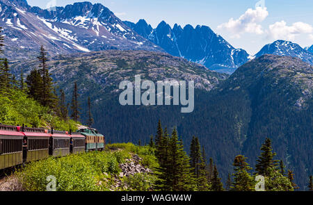 a narrow guage tour train hugs the cliff on the white pass gorge through the mountains near skagway alaska Stock Photo