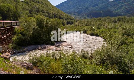 a tourist train on the white pass route crosses over a river running through a mixed forest near skagway alaska Stock Photo