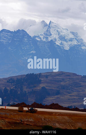 Heavy machinery working moving earth, the start of construction at the site of a new international airport at Chinchero for Cusco and Machu Picchu. In the background is Mt Sawasiray, one of the peaks of the Cordillera Urubamba mountain range. Cusco Region, Peru Stock Photo