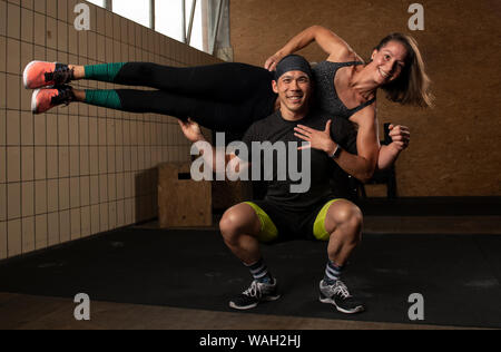 An athletic beautiful couple is smiling, doing a fitness workout together and having fun.The muscular man is holding the fit woman on his shoulders. Stock Photo