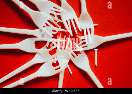 A lot of plastic forks on a red background. The concept of environmental problems, environmental pollution by plastic waste. Top view, close up. Stock Photo