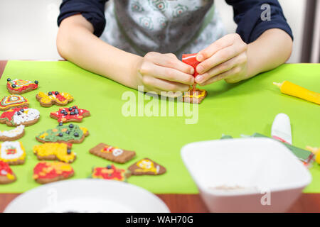 Focussed on the work of the boy's face with glasses and a kitchen apron, which decorates the cookies using icing in a tube. Beautifully decorated cake Stock Photo