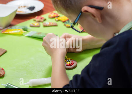Cinnamon cookies lie on the green table. The hands of the child squeeze yellow frosting out of the tube and create decorations. Stock Photo