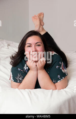 Beautiful real hispanic woman lays and poses relaxed on her bed at home Stock Photo