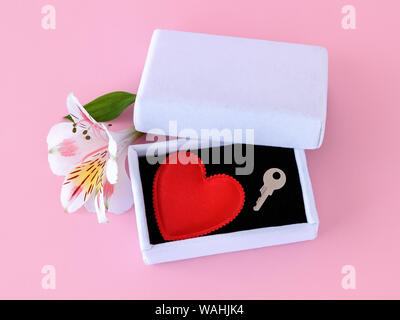 Red silk Valentine heart and a key on black velvet into a white jewelry gift box on a pastel pink background. Key to my heart, to open a heart concept Stock Photo