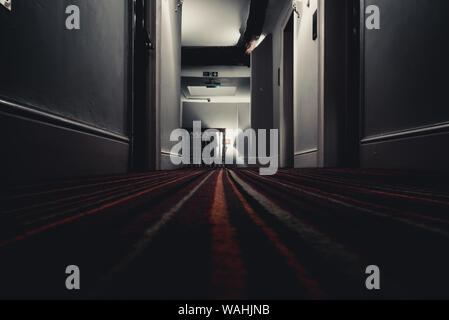 Exit fire sign hanging on ceiling on dark mysterious corridor in building near stairs. Door room perspective in lonely quiet building with creepy Stock Photo