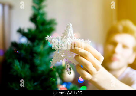 close up person's hands putting white decoration star on top of christmass tree f Stock Photo