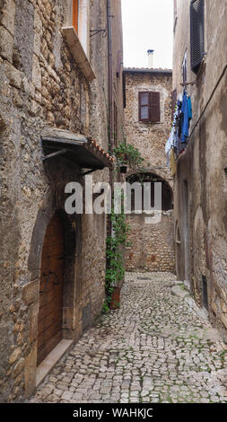 A narrow stone paved street and old medieval houses with arched wooden doors also metal curtains on the windows in small ancient town Sermoneta, Italy Stock Photo