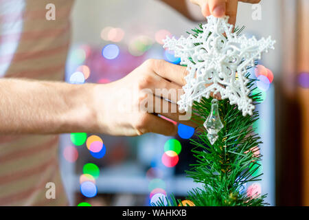 close up person's hands putting white decoration star on top of christmass tree f Stock Photo