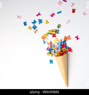 small wooden multi-colored letters of the English alphabet scattered from a conical waffle cup, white background, top view Stock Photo