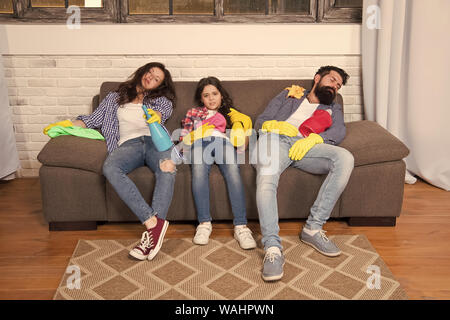 Finish cleaning. Cleaning all day exhausting occupation. Tired parents and kid. Exhausting cleaning day. Family mom dad and daughter with cleaning supplies sit on couch. Family care about cleanliness. Stock Photo