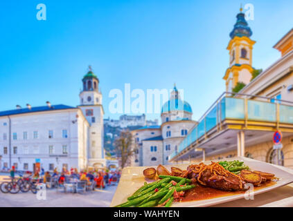 The tasty fried pork with vegetables on the dinner in old Mozartplatz square in historical Salzburg, Austria Stock Photo