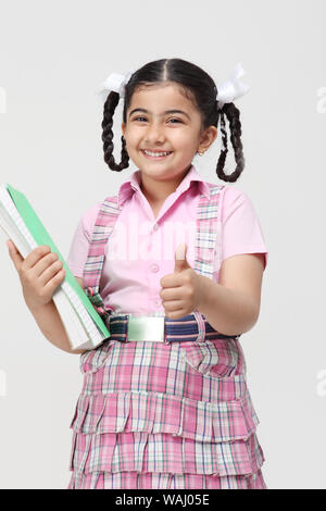 Schoolgirl standing with books and showing thumbs up sign Stock Photo