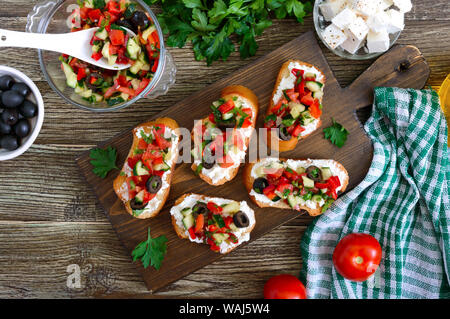 Delicious bruschettas with goat cheese and fresh vegetables. Crispy baguette slices with feta, tomatoes, cucumbers, peppers, olives, herbs. Healthy br Stock Photo