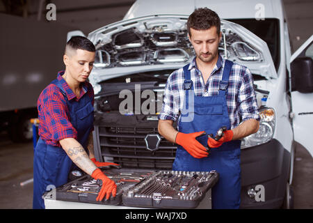 Two people working at the car repair workshop together as they fix the mechanical part of it with the help of numerous instruments. Stock Photo