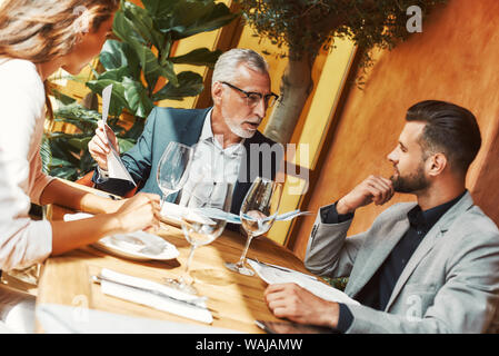 Cropped portrait of three colleagues talking about their plans while sitting in a restaurant. Glasses of wine on the table. Horizontal shot Stock Photo