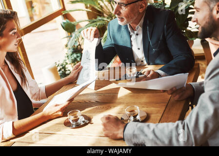 Cropped portrait of three colleagues talking about their plans while sitting in a restaurant. Coffee cups on the table. Horizontal shot Stock Photo