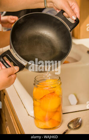 Woman pouring hot syrup mixture (sugar and water mixture) into a jar of peach halves until the peaches are covered and ready to be canned. (MR) Stock Photo