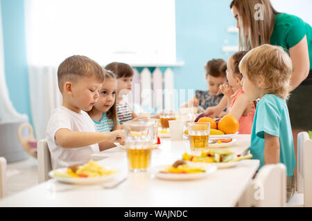 Kids have a dinner in kindergarten. Little boys and girls from the group of children sitting at table with lunch and eat appetizing. Children with car Stock Photo