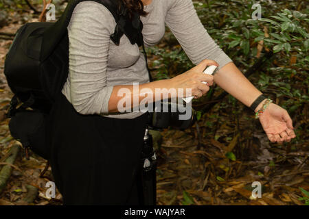 Woman spraying mosquito insect repellent on her arm in tropical forest. Stock Photo