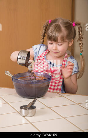Girl pouring chocolate chips into a chocolate bundt cake in mixing bowl. (MR, PR) Stock Photo