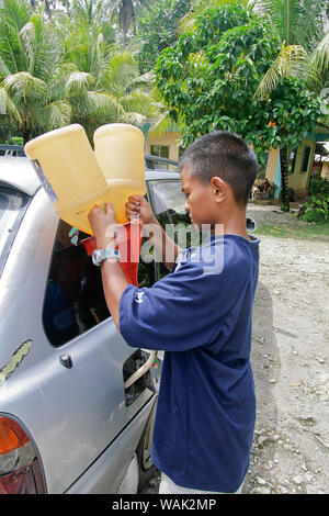 Kosrae, Micronesia (FSM). Young boy filling local car with gasoline from gallon jugs. This is how gasoline is sold on Kosrae. (Editorial Use Only) Stock Photo