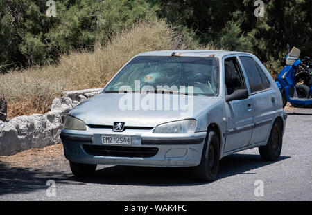 Perissa, Greece - July 11 2019:   A Peugeot car with a smashed windscreen sits abandoned on the sea front road Stock Photo