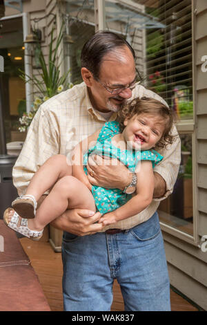 Issaquah, Washington State, USA. Grandfather playfully holding his eighteen month old granddaughter on the deck of his backyard. (MR,PR) Stock Photo