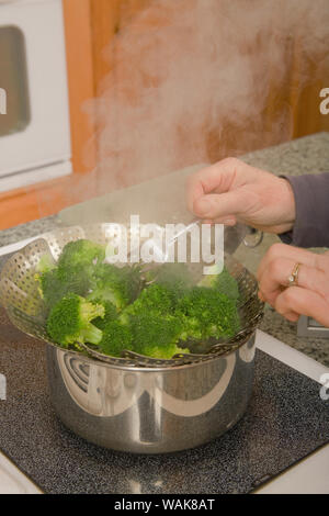 Woman removing a strainer of blanched, chopped broccoli out of a pan in preparation for freezing. (MR,PR) Stock Photo