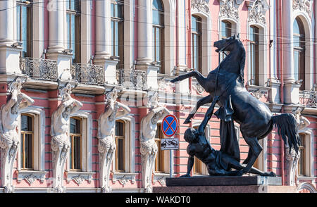 One of four iconic horse sculptures “The Horse Tamers” on Anichkov Bridge with the Belosselsky Belozersky Palace in the background, Saint Petersburg, Stock Photo