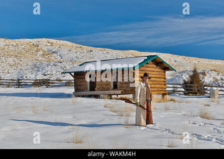 Cowboy horse drive on Hideout Ranch, Shell, Wyoming. Cowboy with rifle in snowfield with log cabin. (MR) Stock Photo