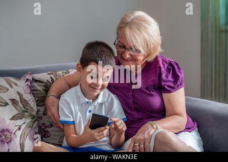 Attentive grandma pointing finger in mobile. Smiling boy keeping it in hand. Communication and technology concept Stock Photo