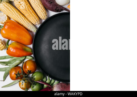 Pattern made of vegetables. Food concept. Tomatoes, carrot, garlic, red beet, pepper, zucchini, corn, green haricot and black plate on white backgroun Stock Photo