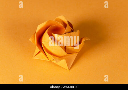 Orange origami rose on orange background. Japanese art of paper folding. Flat square sheet of paper transferred into a finished sculpture. Stock Photo