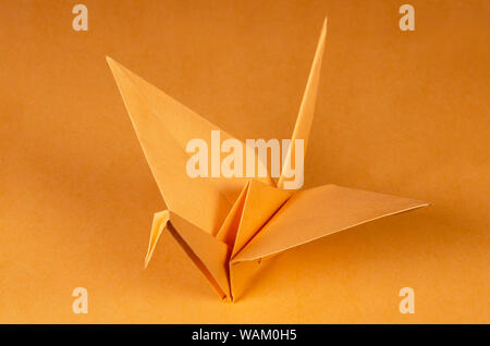 Orange origami crane on orange background. Tsuru. Japanese art of paper folding. Flat square sheet of paper transferred into a finished sculpture. Stock Photo
