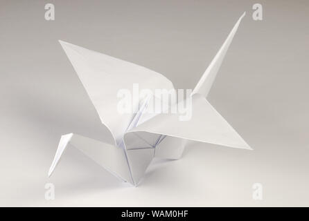 Light gray origami crane on gray background. Tsuru. Japanese art of paper folding. Flat square sheet of paper transferred into finished sculpture. Stock Photo