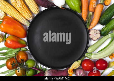 Pattern made of autumn vegetables. Tomatoes, onion, cucumber, carrot, garlic, red beet, pepper, zucchini, corn, green haricot and black plate on white Stock Photo