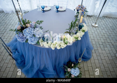 Wedding table decorated with white flowers, candles. Soft sofa with cushions, large window.Blue and white. Stock Photo