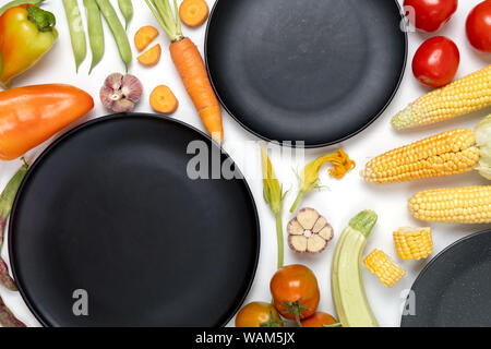 Creative layout made of autumn vegetables. Tomatoes, onion, carrot, garlic, red beet, pepper, zucchini, corn, green haricot and black plate on white b Stock Photo