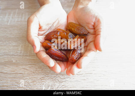 hand holding dried fruits from date palm on wooden background, phoenix dactylifera in hand. Stock Photo