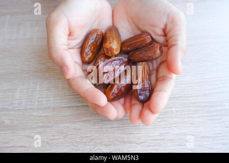 hand holding dried fruits from date palm on wooden background, phoenix dactylifera in hand. Stock Photo
