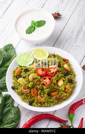 Palak Paneer Biryani and Raita at white wooden background with decor. Palak Paneer Biryani is vegetarian indian cuisine dish with spinach, paneer , ba Stock Photo