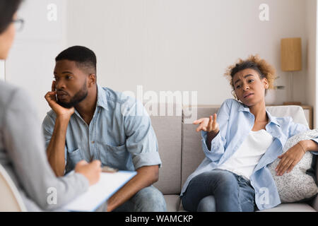 Afro Husband Looking Away While Wife Complaining To Marital Counselor Stock Photo