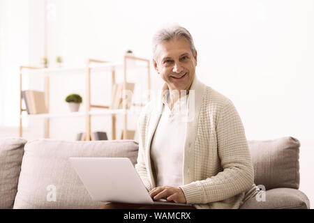 Mature man surfing internet on laptop and looking at camera Stock Photo