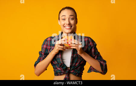 Slim Girl Eating Burger Over Yellow Studio Background Stock Photo