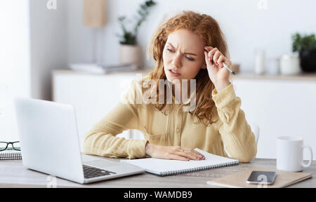 Bored woman with laptop and paperwork making notes Stock Photo