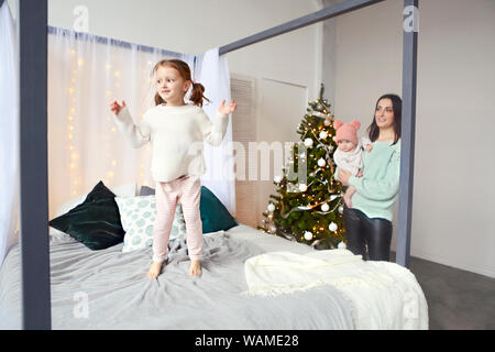 Beautiful happy mother with lher ittle daughter in knit sweater sitting on the background of Christmas interior hugging together and smiling Stock Photo